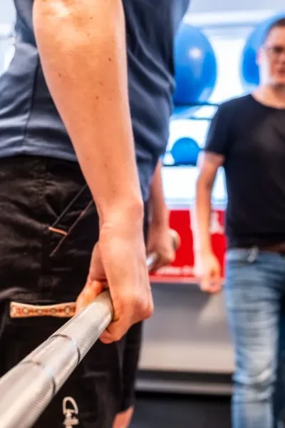Trainer che segue un cliente durante l'allenamento di forza con il bilanciere in palestra.