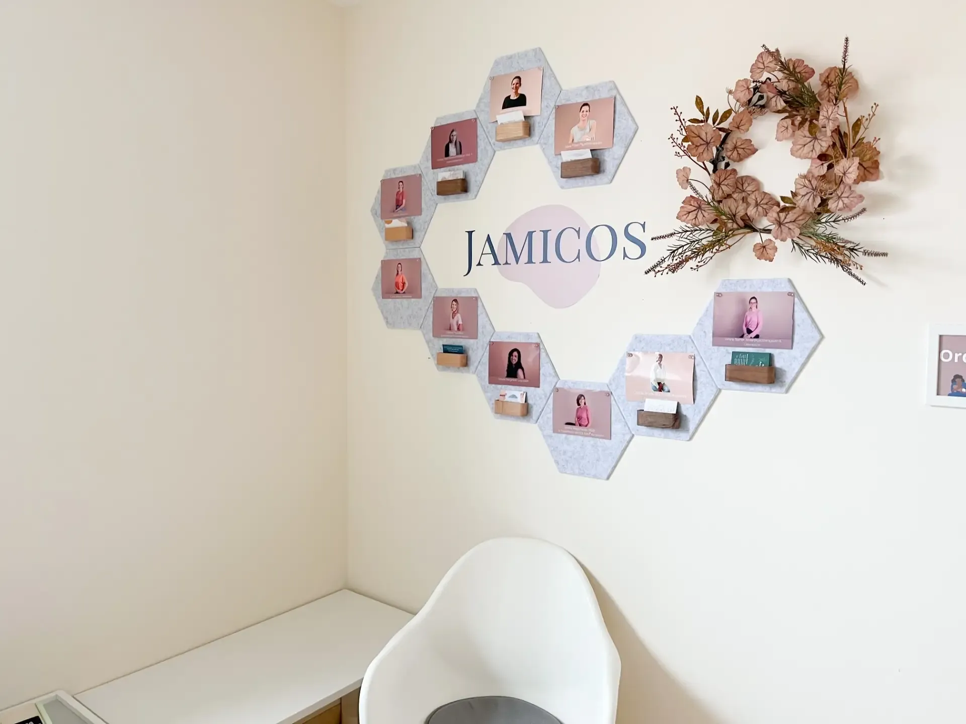 Wall with hexagonal team portrait frames arranged around the JAMICOS logo, next to an autumn floral wreath.