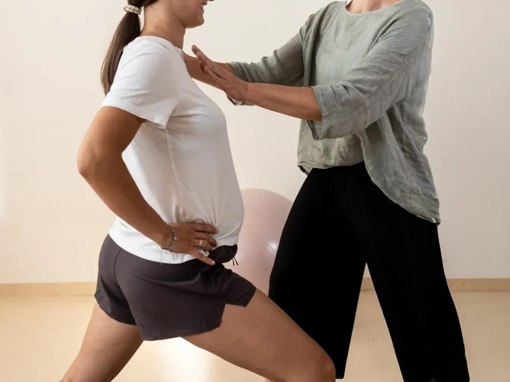 Course instructor assisting a pregnant woman with a lunging stretch exercise